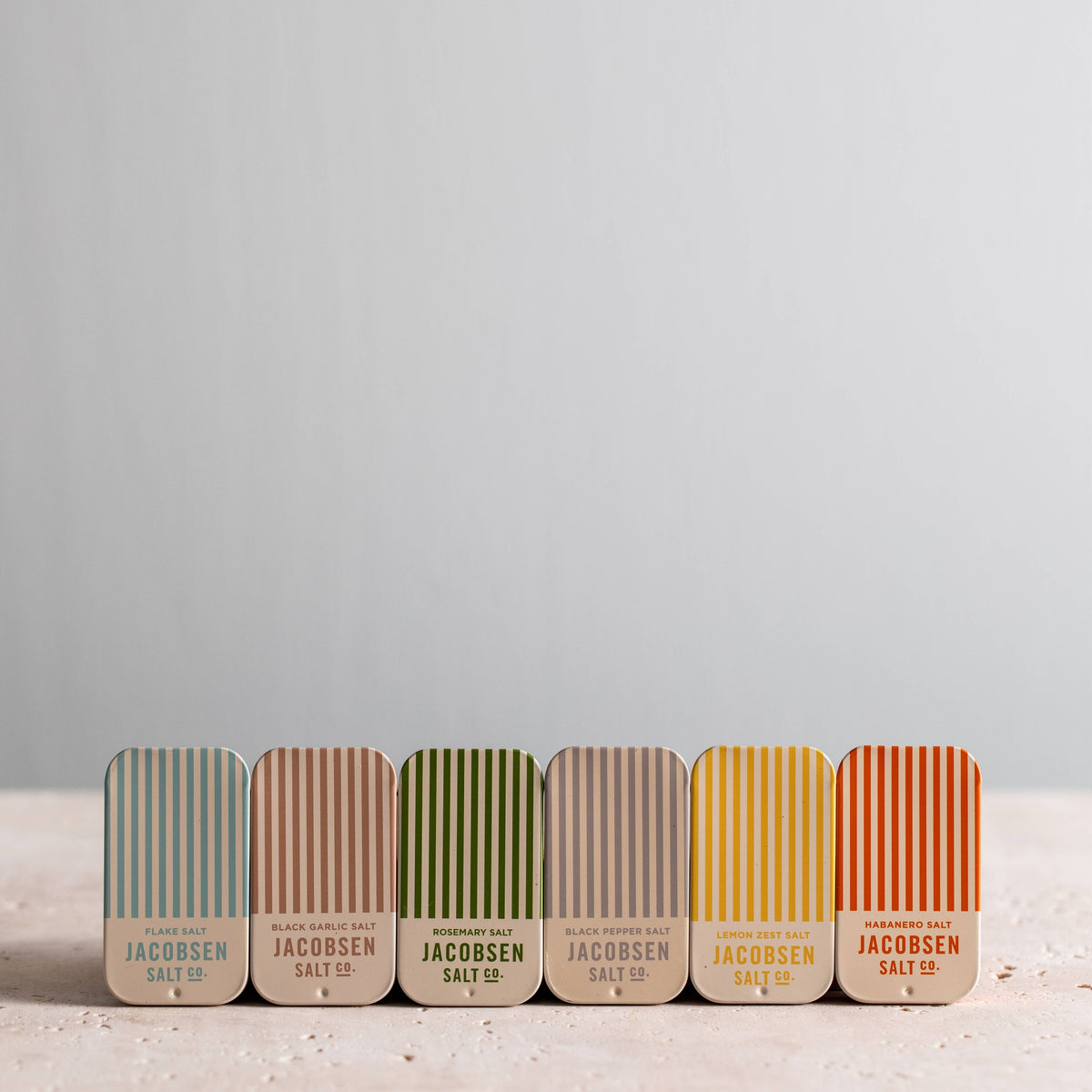 Row of Jacobsen Salt Co. salt tins in various colors on a light background
