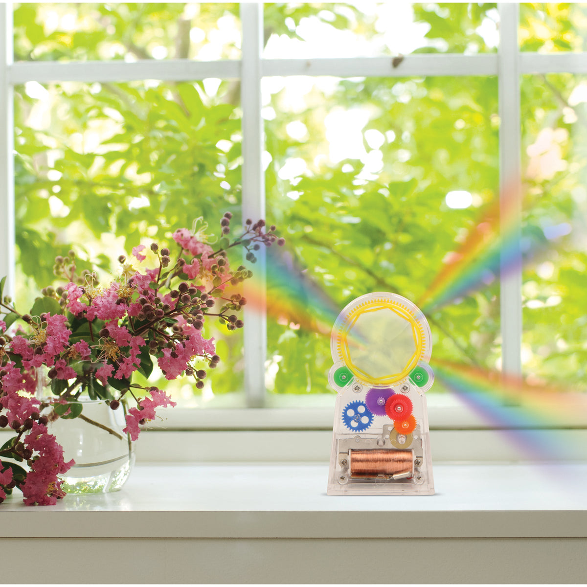 Colorful gear toy with a rainbow on a windowsill with flowers and greenery outside.