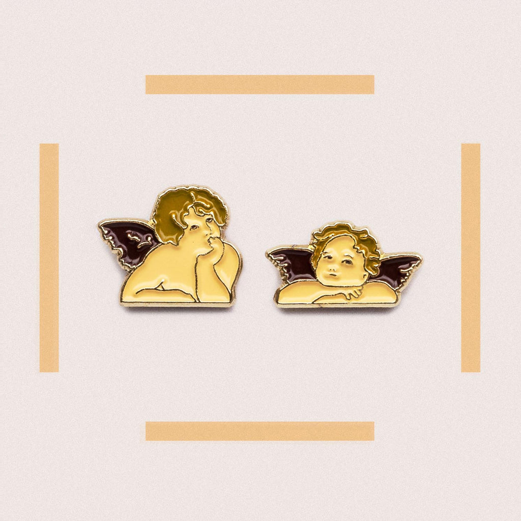 Two angel pins on a light pink background