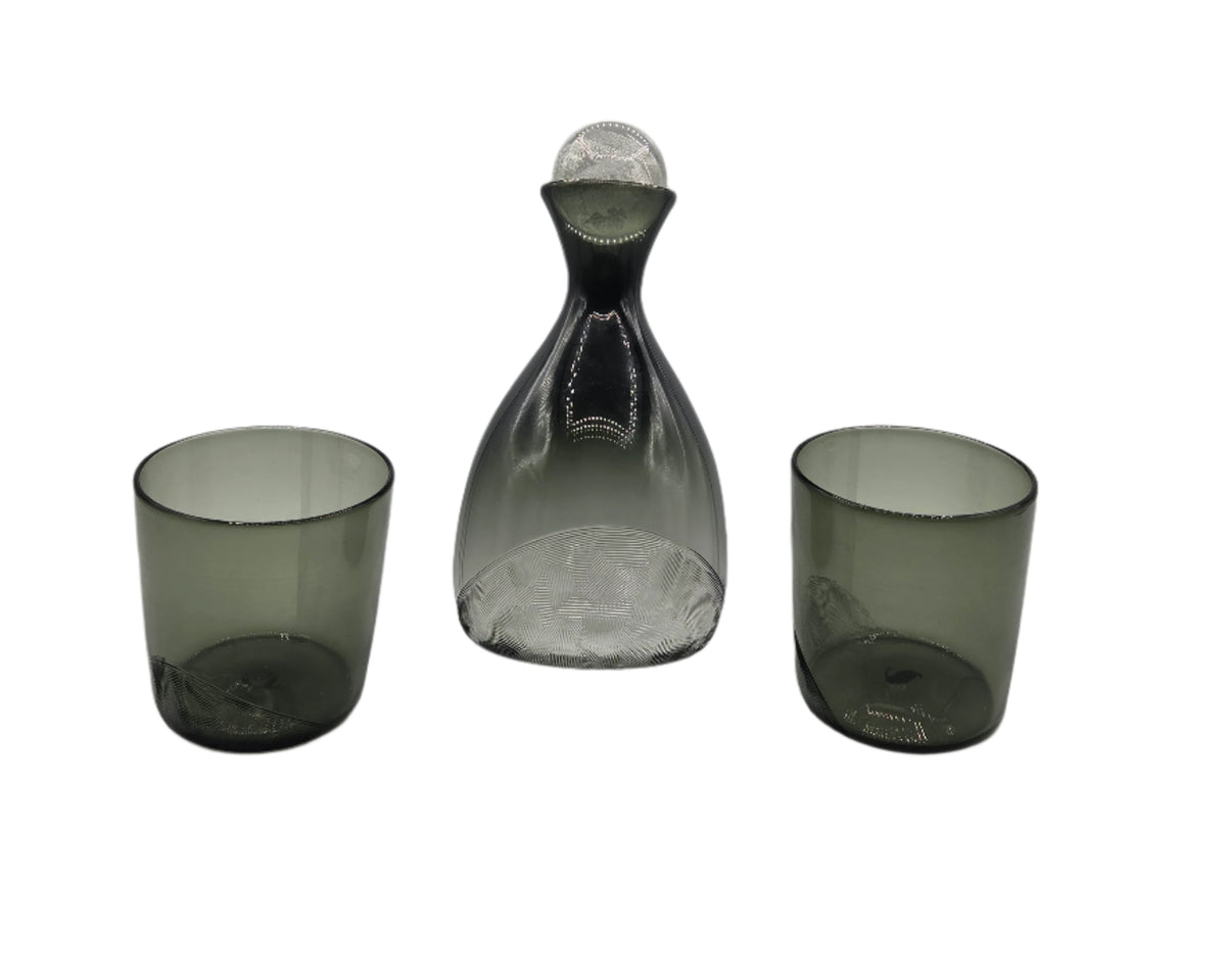 Set of three smoked glass pieces including a decanter and two tumblers on a white background