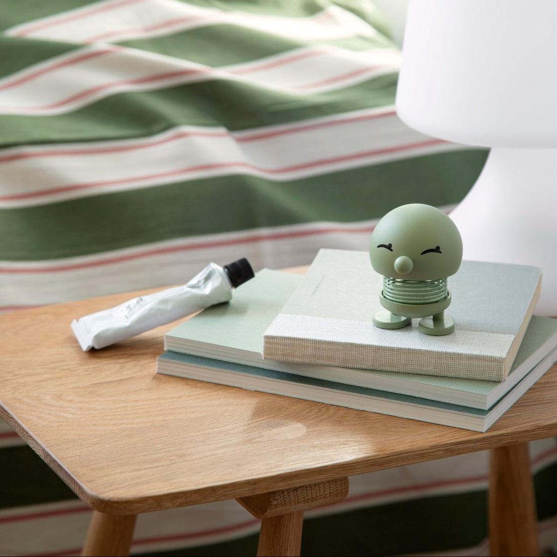 Small green figurine on a stack of books with a striped fabric background