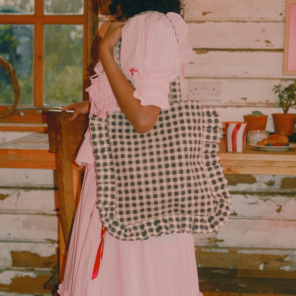 Person wearing a pink checkered dress with a black and white checkered bag in a rustic setting.