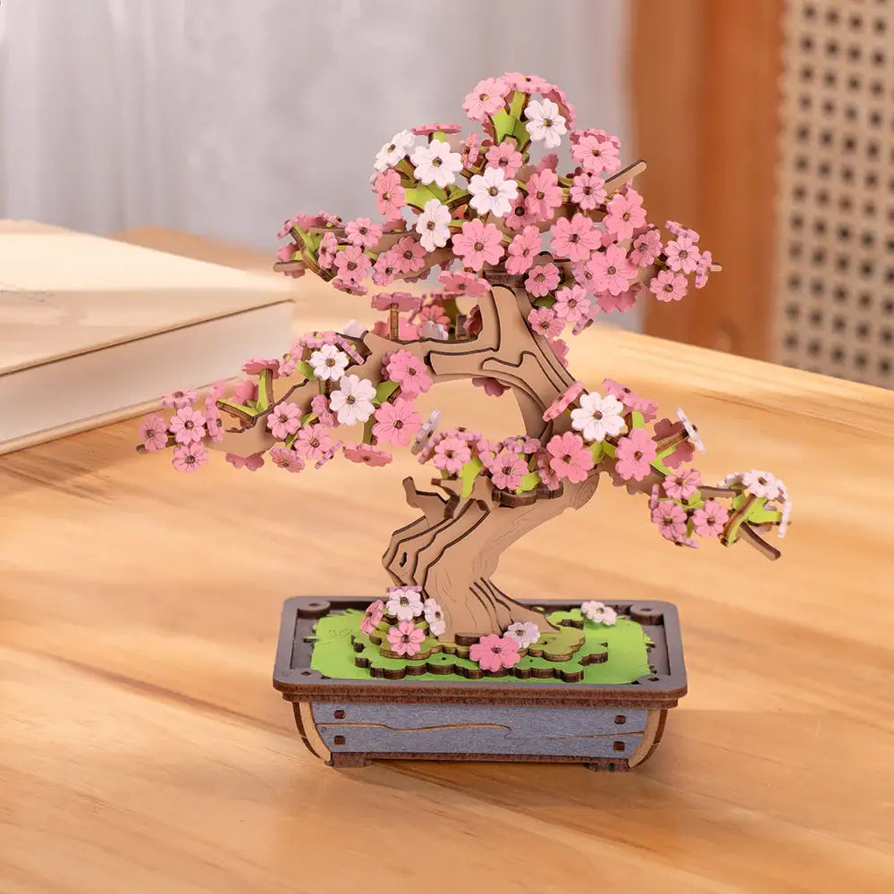 Wooden bonsai tree model with pink and white flowers on a wooden surface