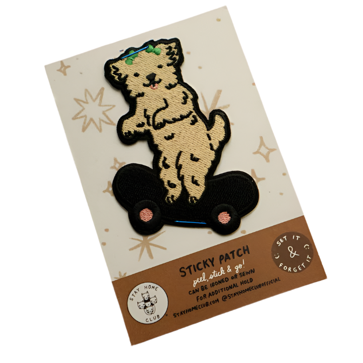 A packaged embroidered patch featuring a cartoon dog character riding a skateboard, with a sticky patch backing, displayed on a card with the brand 'STICKY PATCH'.