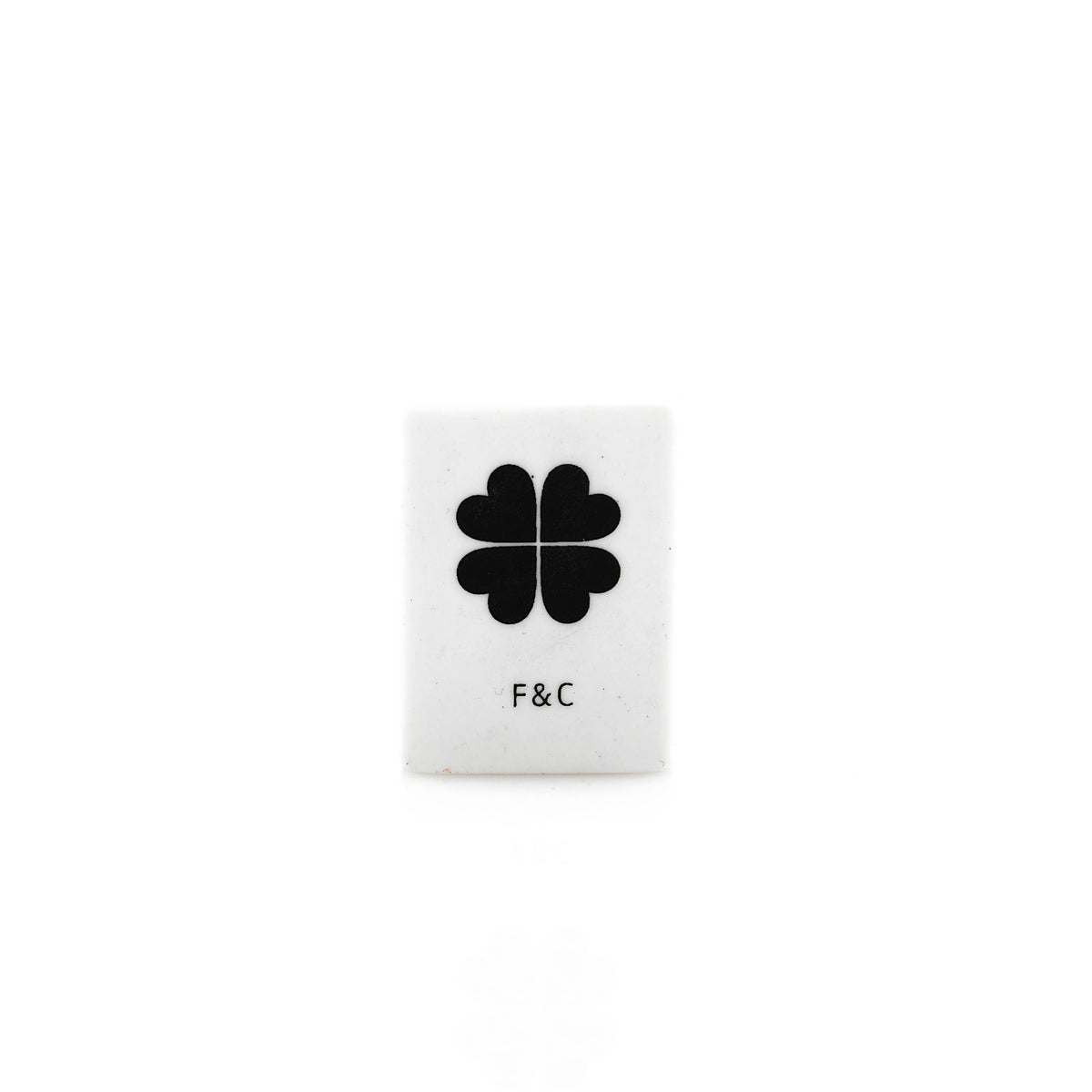 Small white eraser with a black four-leaf clover design and &#39;F&amp;C&#39; text on a white background