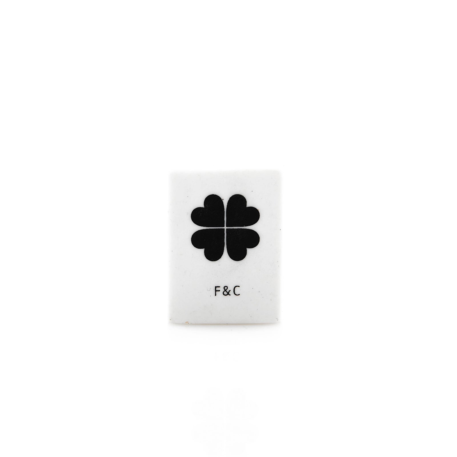Small white eraser with a black four-leaf clover design and 'F&C' text on a white background