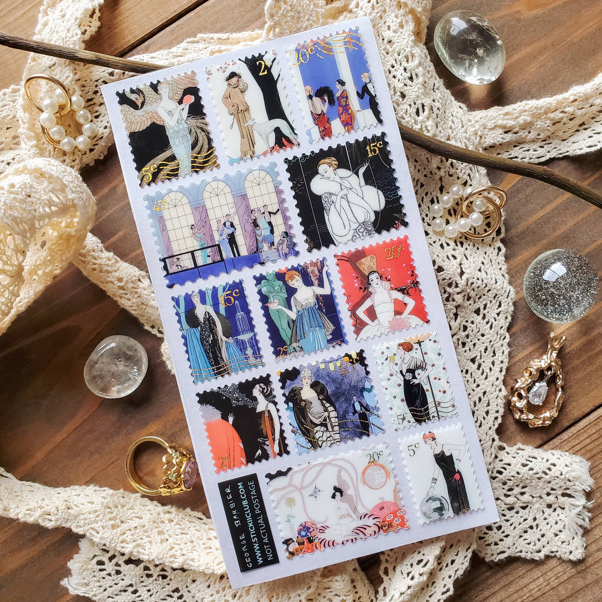 Sheet of decorative stamps featuring vintage-style illustrations on a wooden surface with lace and jewelry.