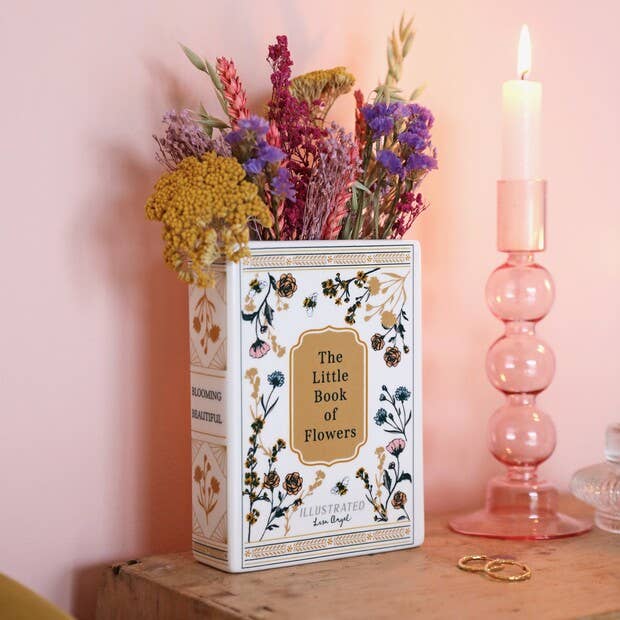 Book titled 'The Little Book of Flowers' with a floral design, placed on a wooden surface with flowers and a candle in the background.