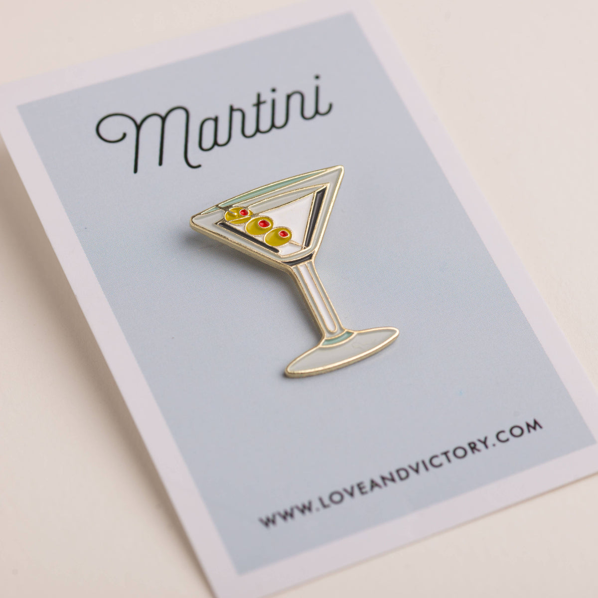 Martini-themed enamel pin on a card with &#39;Love and Victory&#39; branding.