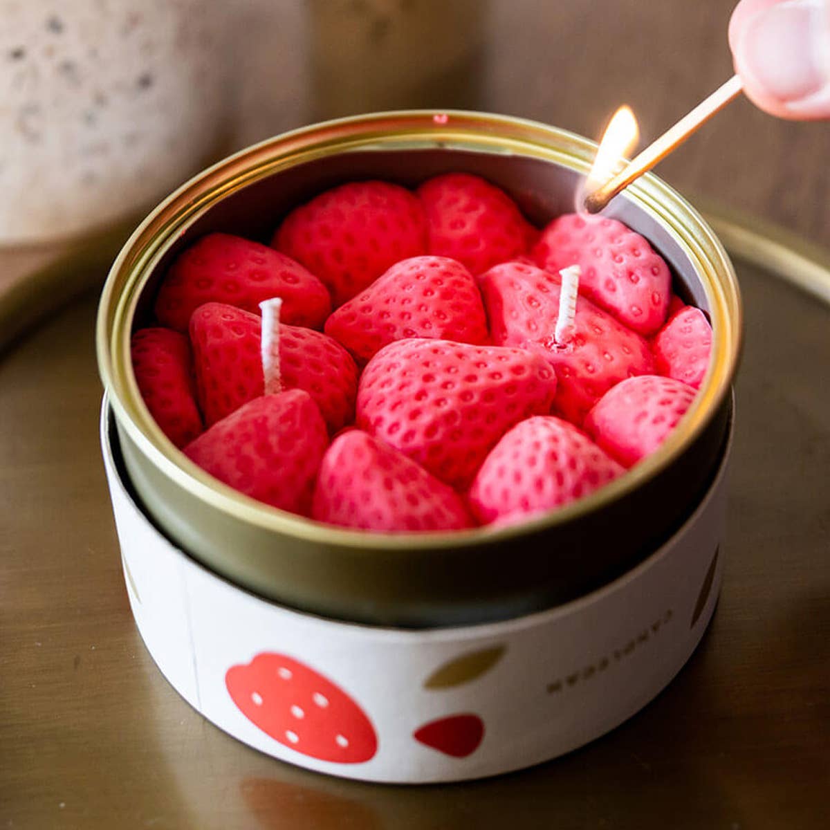 Strawberry-shaped candles in a tin with a lit match