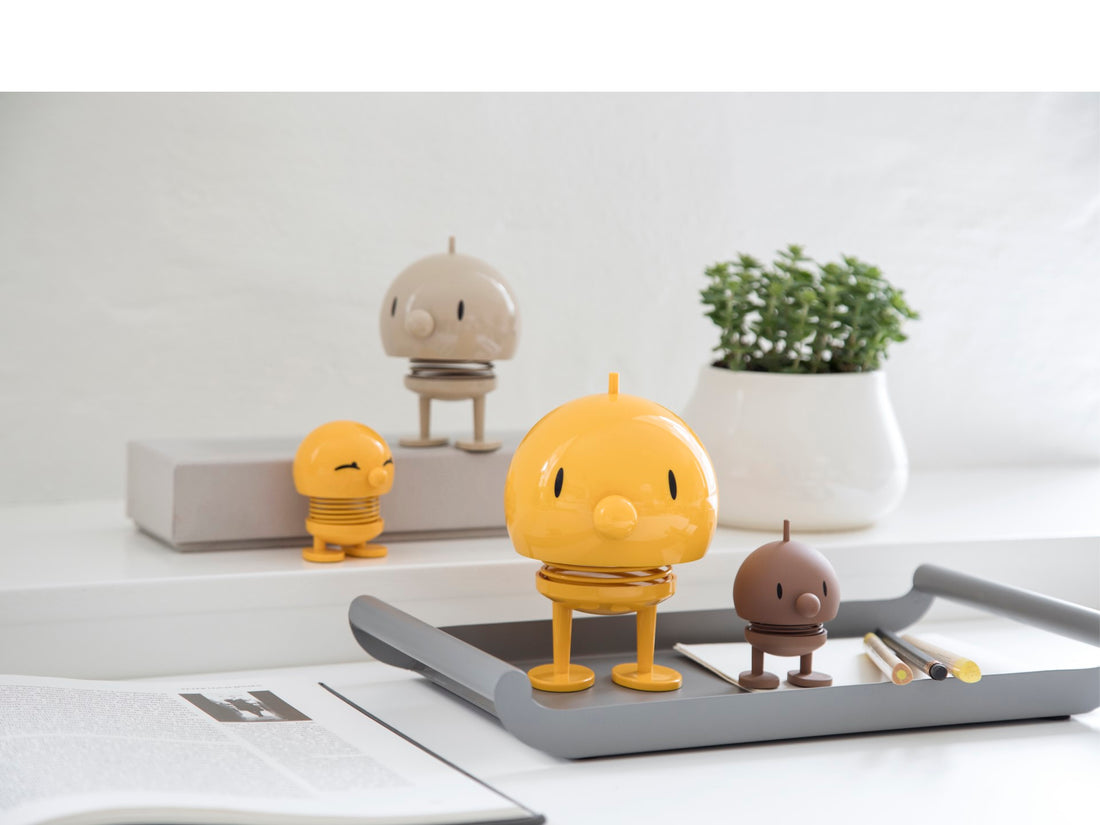 Yellow character figurine on a tray with other small figurines and a plant in the background.