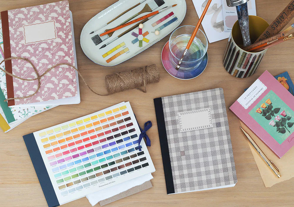 Desk with stationery items including notebooks, paint swatches, and art supplies.