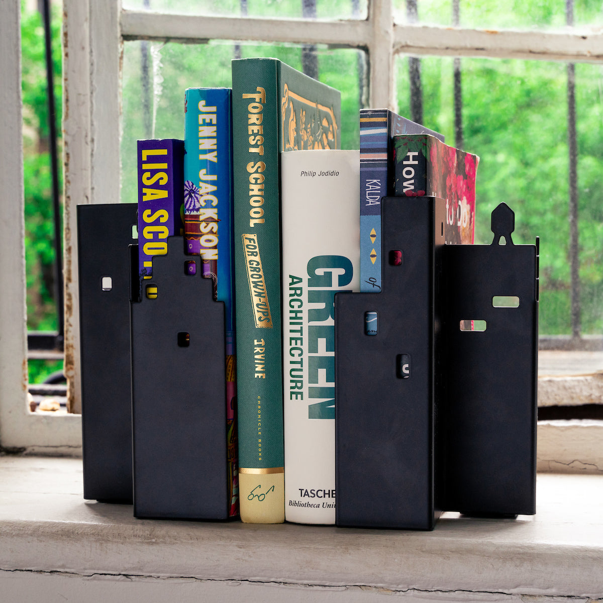 Stack of books with decorative black bookends on a windowsill with a view outside.