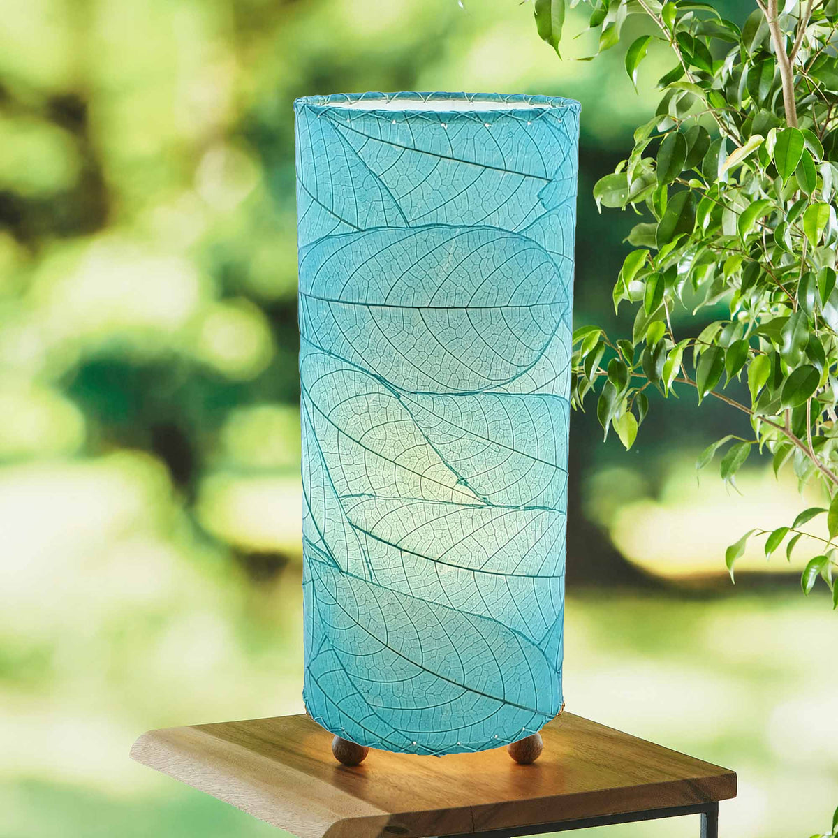 Blue leaf lamp on a table outside with trees in the background