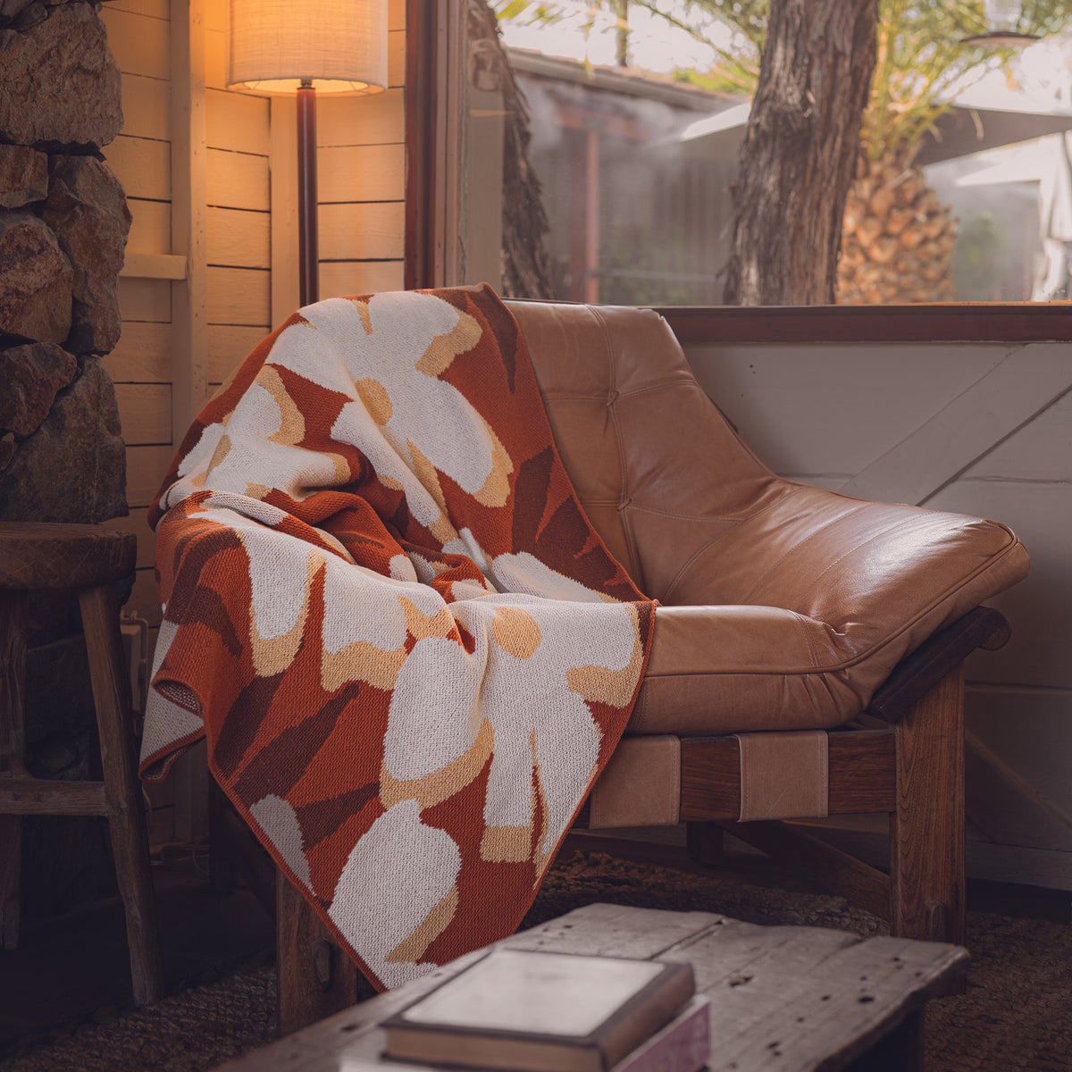 Brown leather chair with a large floral patterned orange and white blanket draped over it, in a cozy room setting.