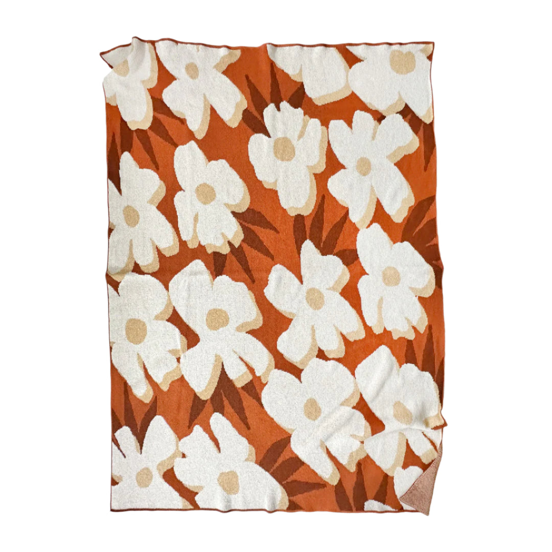 Floral patterned blanket with white flowers on a rust background