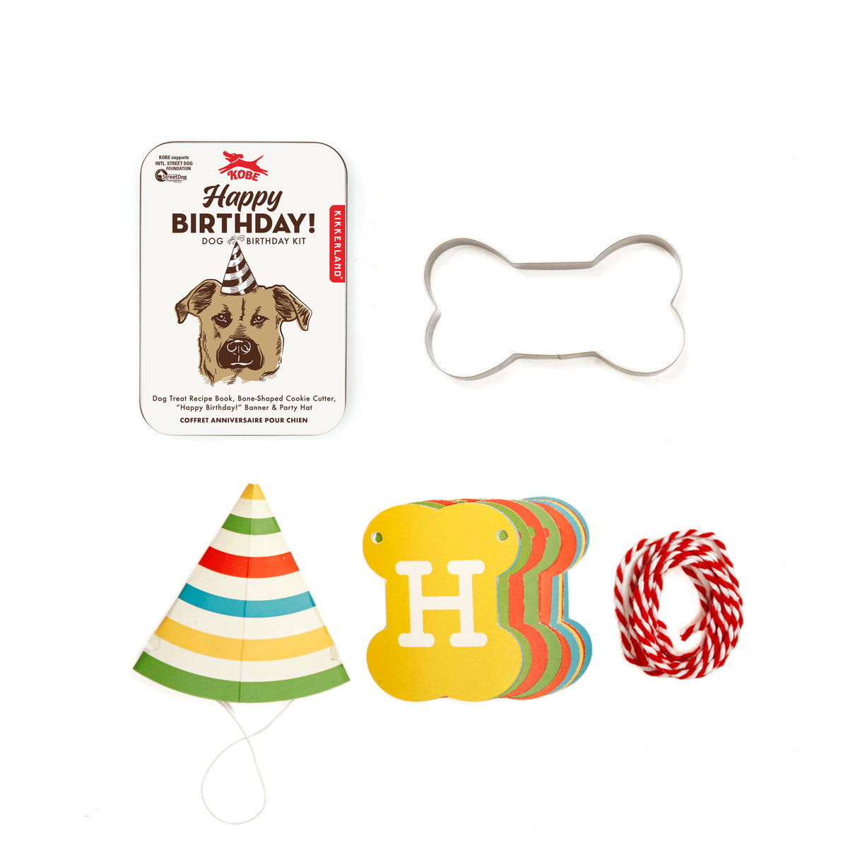 Dog birthday party kit with cake, hat, bone cookie cutter, and other supplies on a white background
