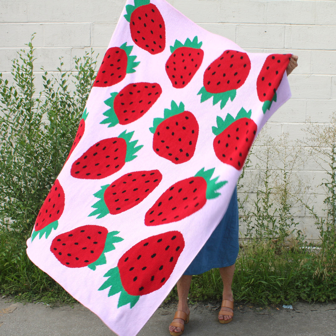 Person holding a strawberry-patterned blanket against a white wall.