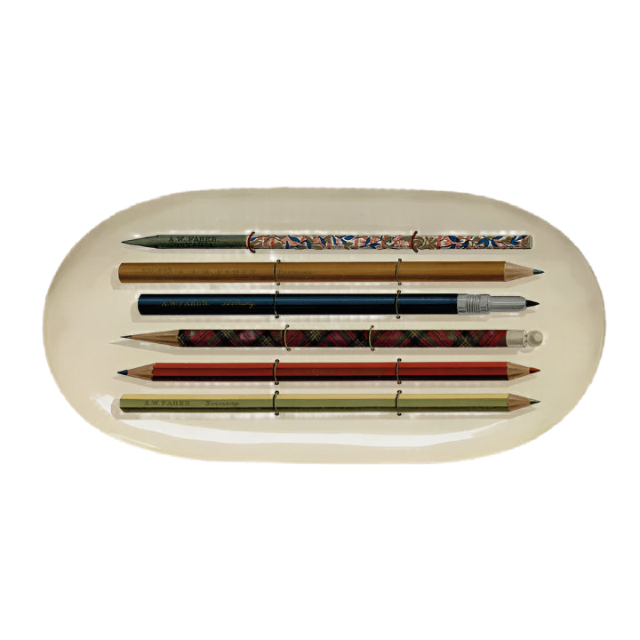 Set of six pencils with decorative grips on a beige oval tray against a light gray background