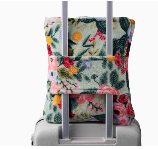 Floral-patterned blanket strapped on suitcase handle on a white background