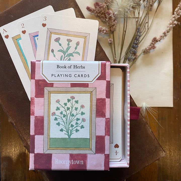 Playing cards with &#39;Book of Herbs&#39; design in a box, featuring illustrations of plants.
