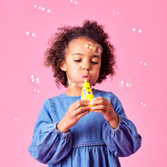 Child blowing bubbles against a pink background