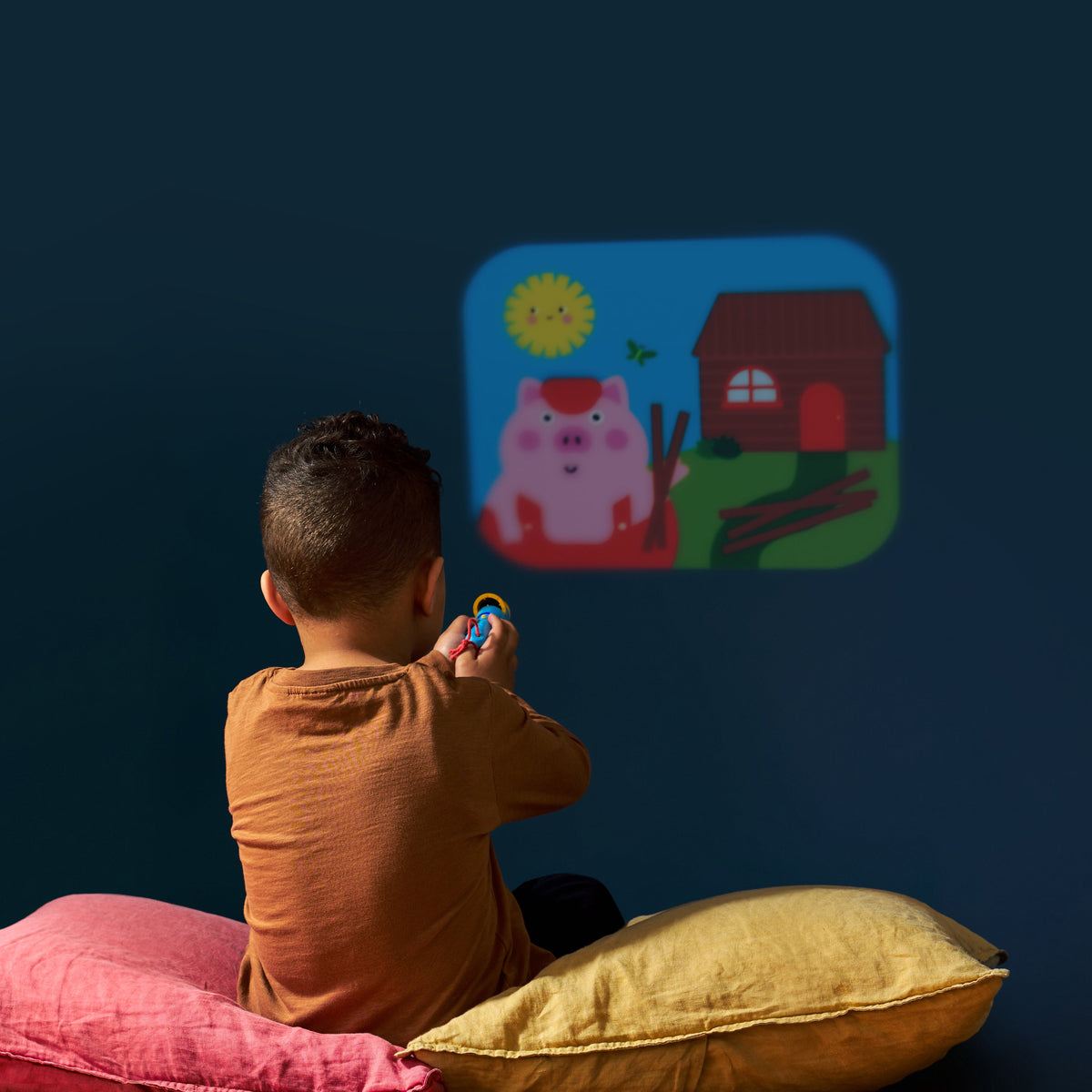 Child sitting on a pillow watching a colorful cartoon projection on a dark wall.
