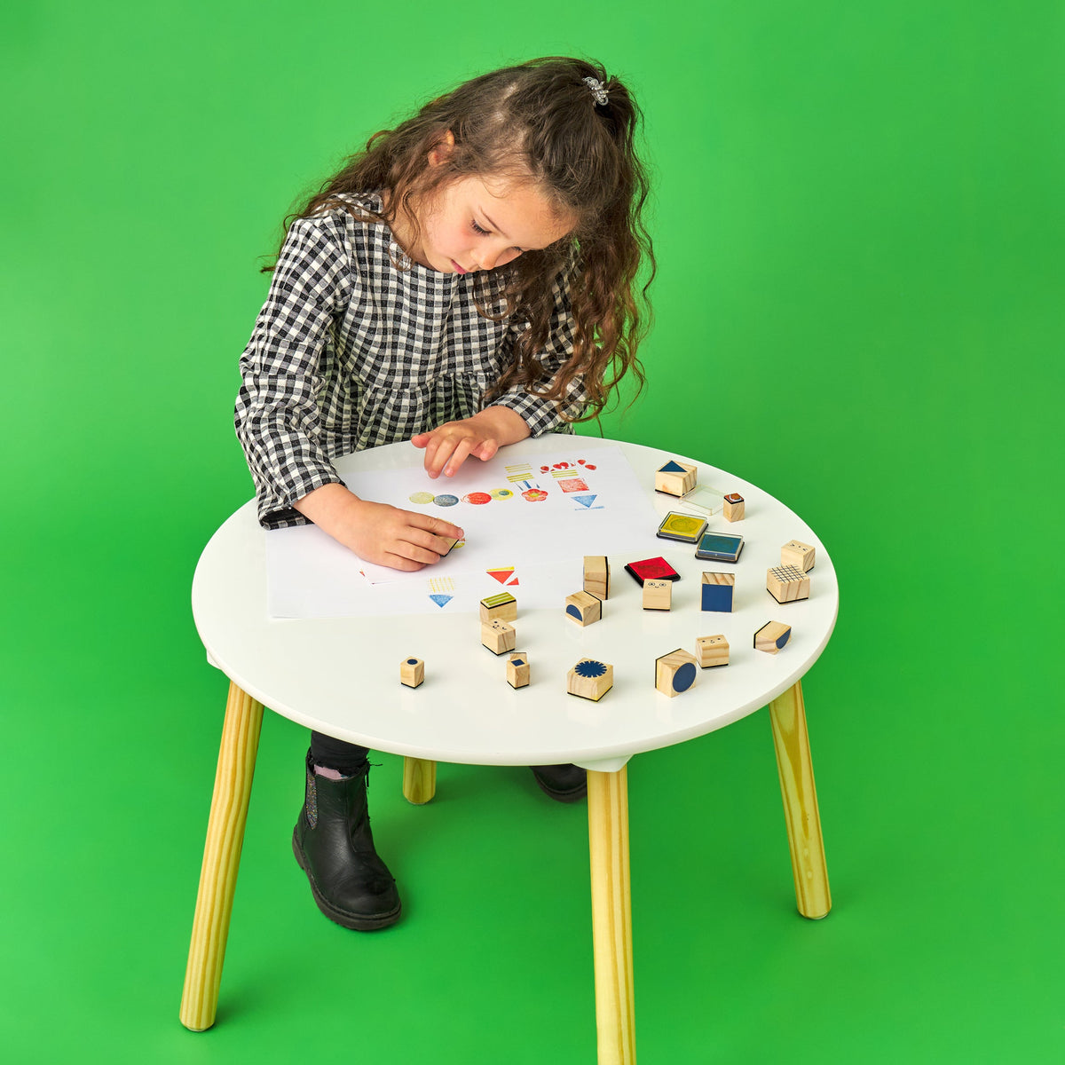 Child playing with colorful block stamps on a round table against a green background