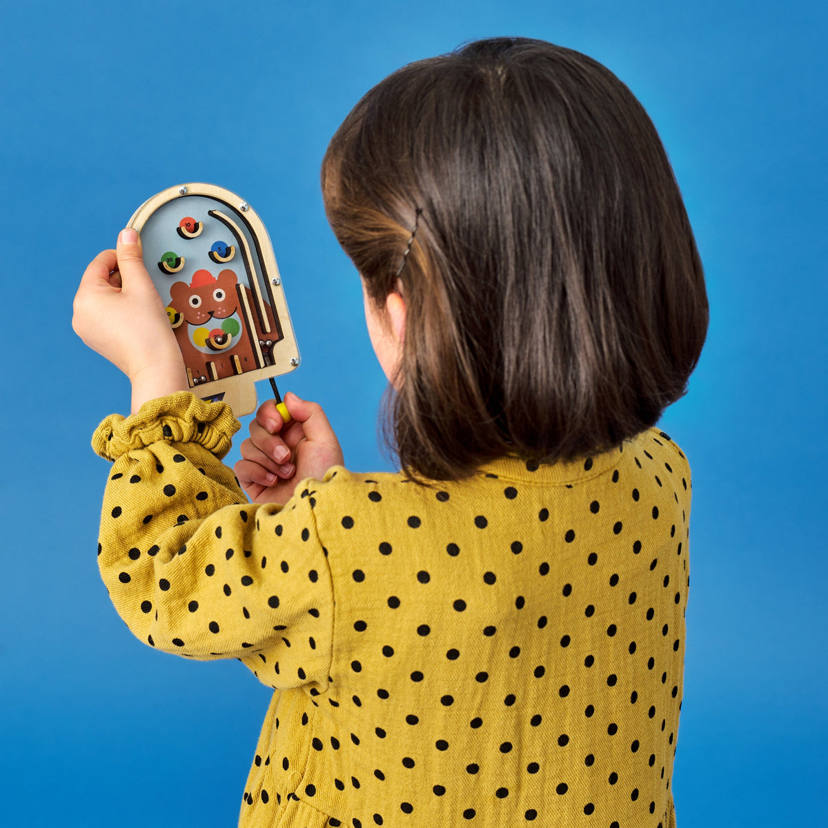 Child in yellow polka dot shirt holding a wooden toy with colorful design against a blue background