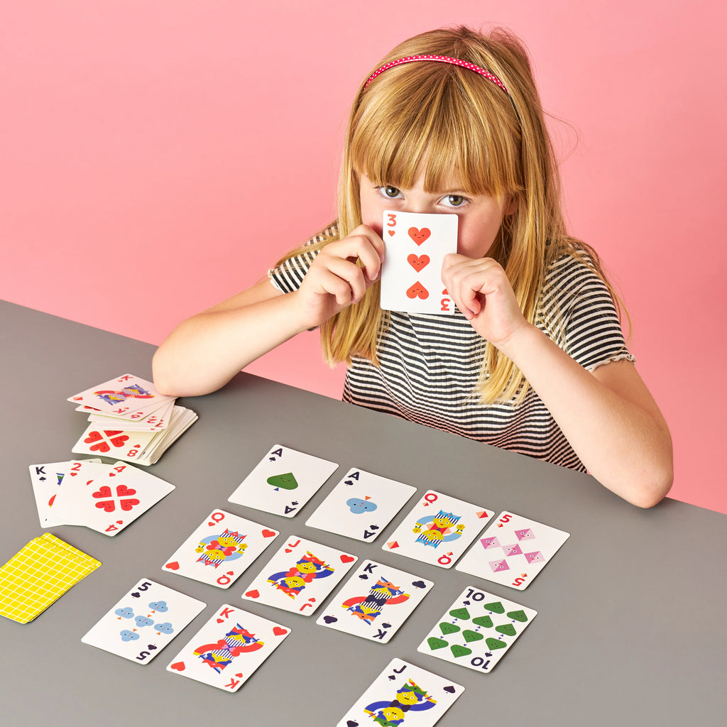 Young girl playing with colorful playing cards on a gray table against a pink background