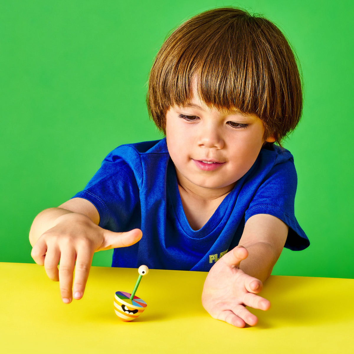 Child playing with a spinning top on a yellow table against a green background