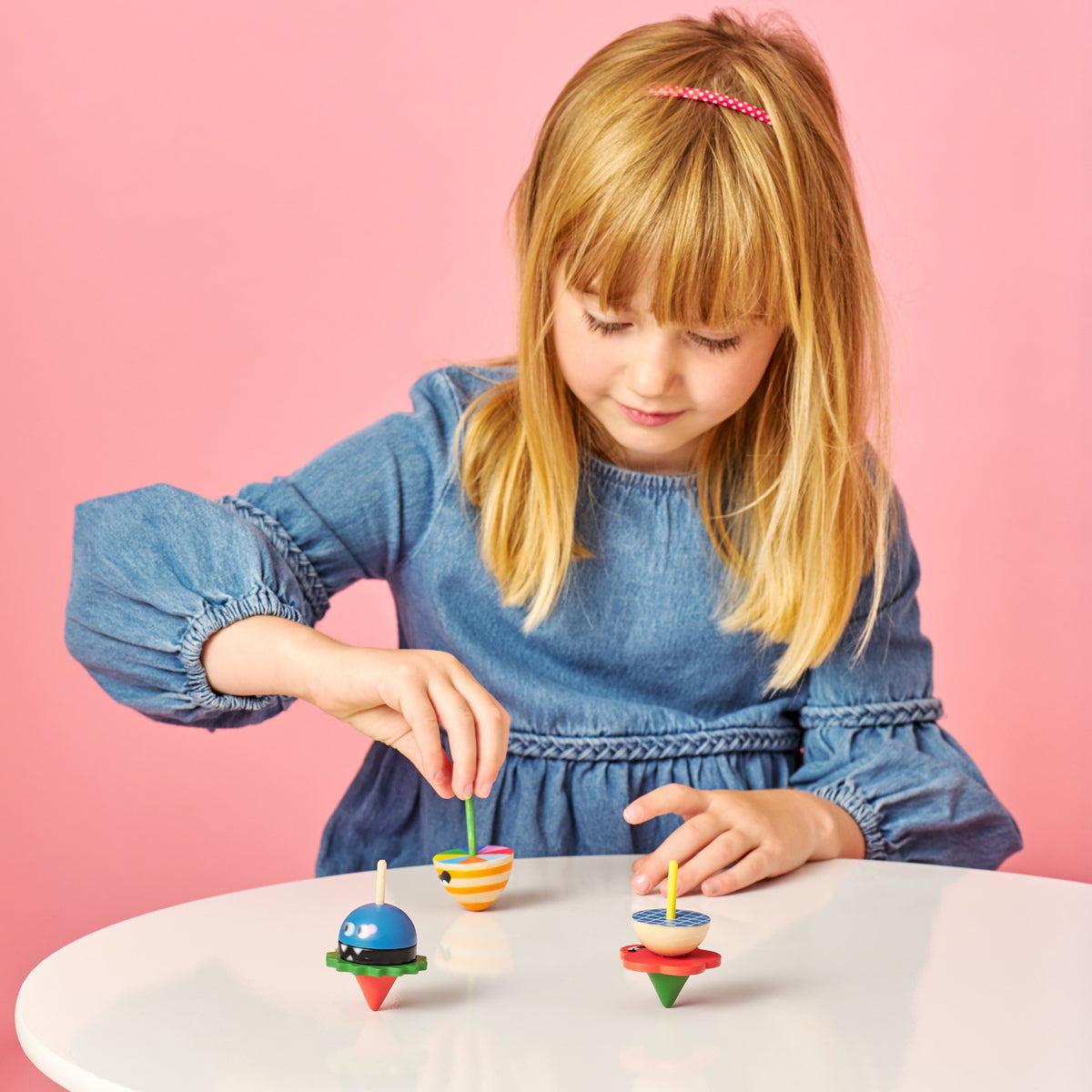 Young girl playing with colorful spin tops on a pink background