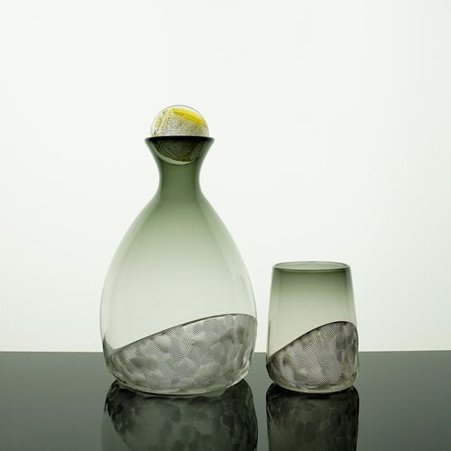 Glass decanter and tumbler with textured design on a reflective surface