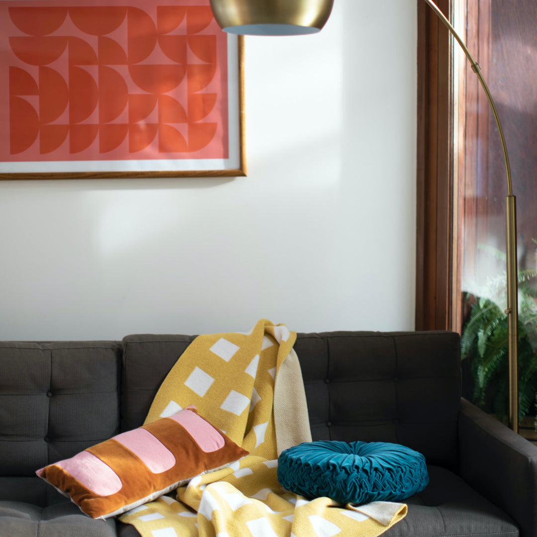 Living room with a gray sofa, colorful pillows, and a red abstract painting on the wall. Yellow and white checkered blanket draped on the sofa