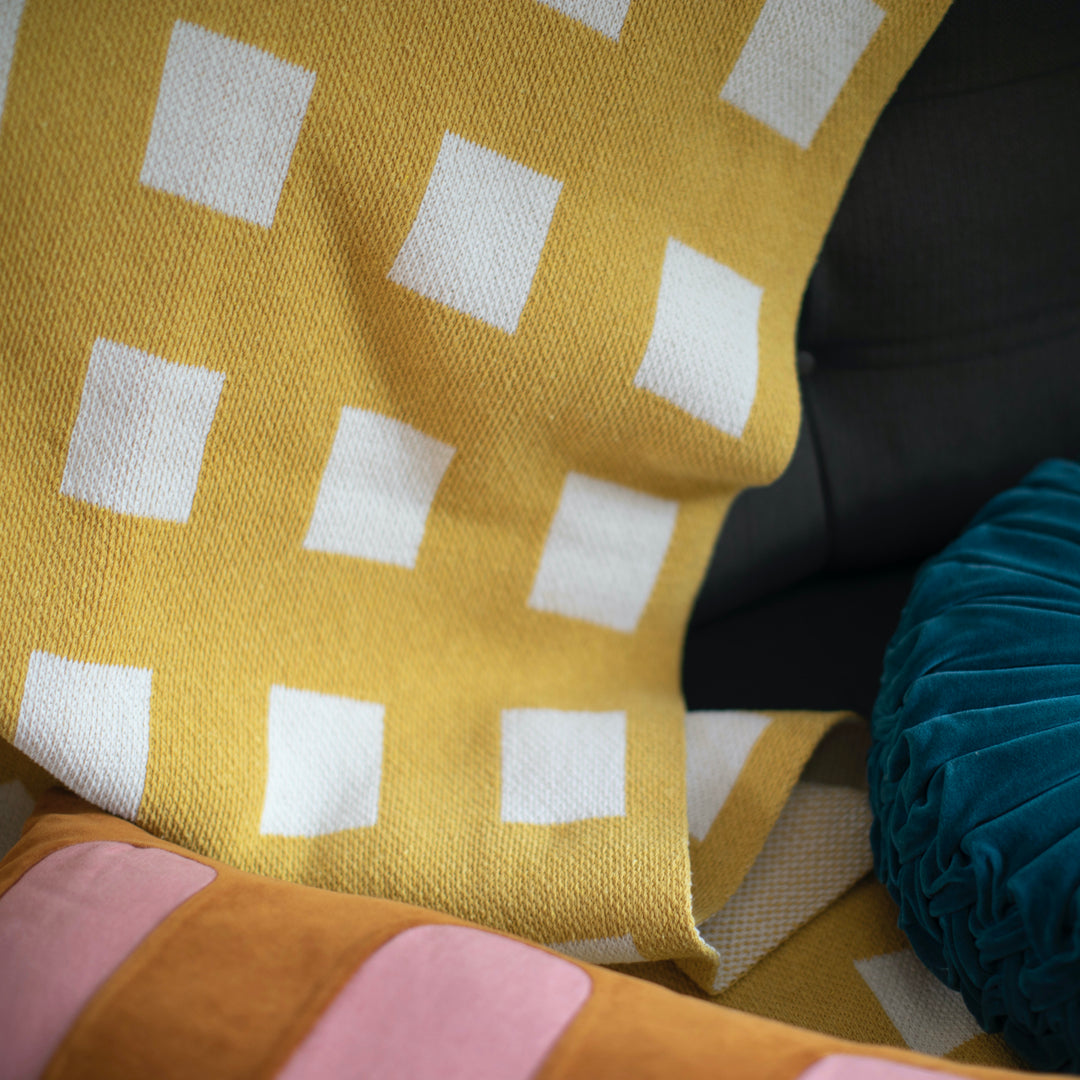 Close-up of a yellow and white checkered blanket with a pink pillow and teal round pillow in the background.