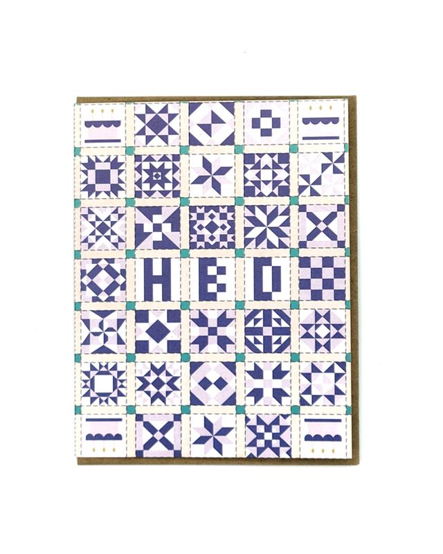 A folded greeting card with a patchwork quilt pattern in blue and white colors, displaying the text 'HBD' on the front, presented in a cello sleeve with an envelope.