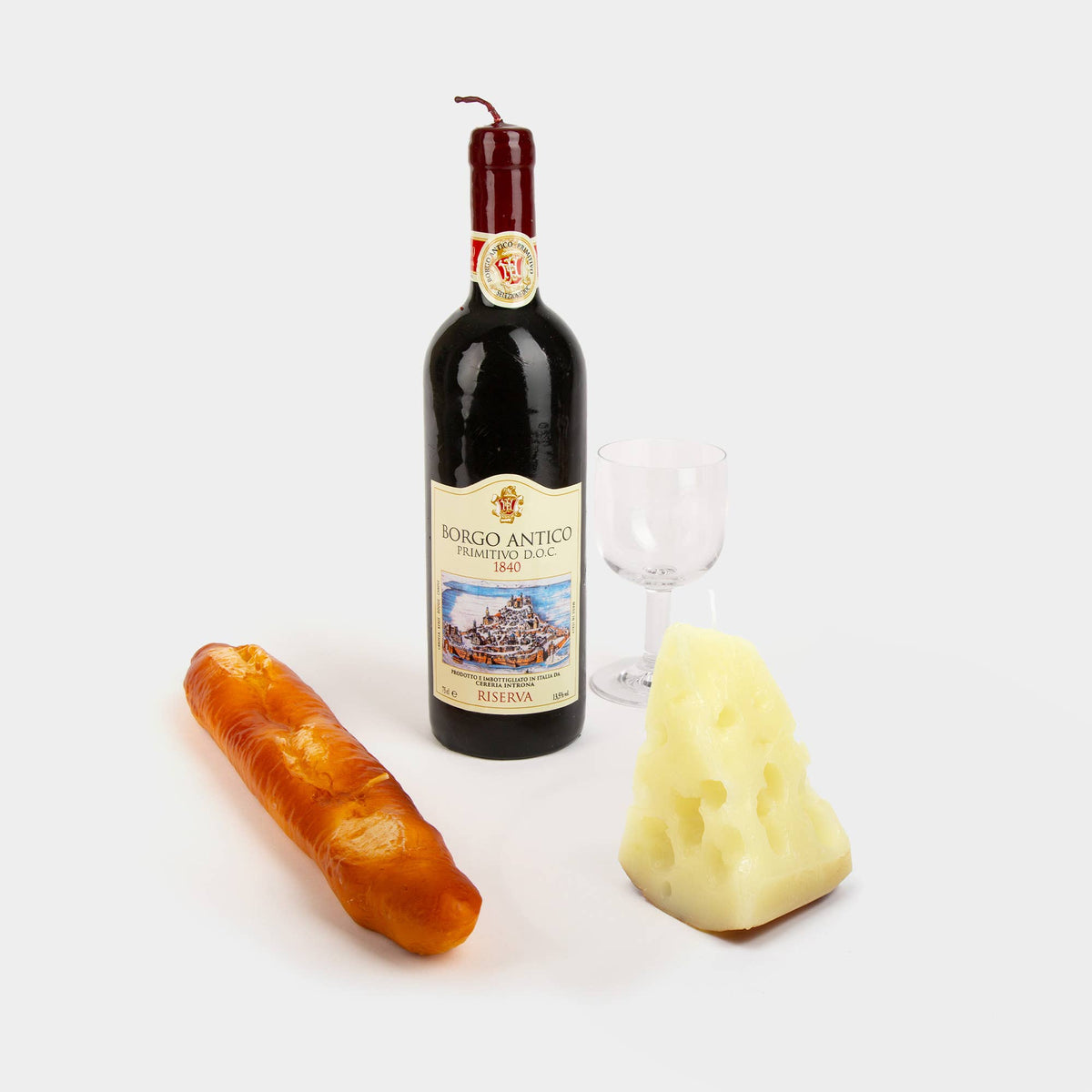 Bottle of wine candle with a label, a loaf of bread candle, and a block of cheese candle on a white background