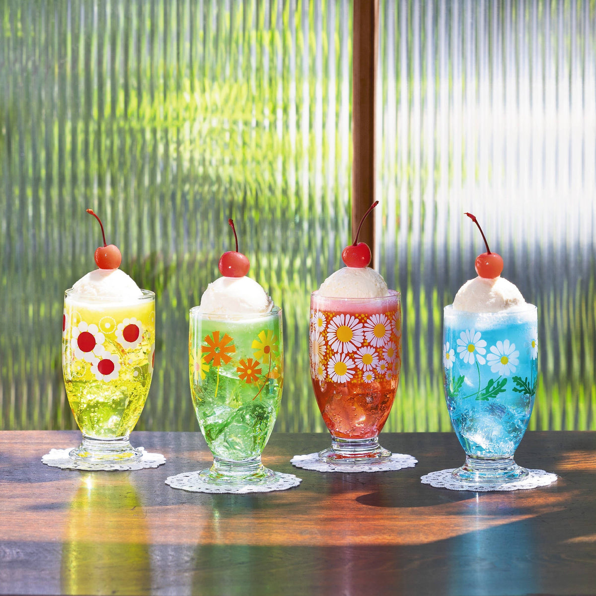 Four colorful milkshakes with floral and fruit decorations on a wooden surface.