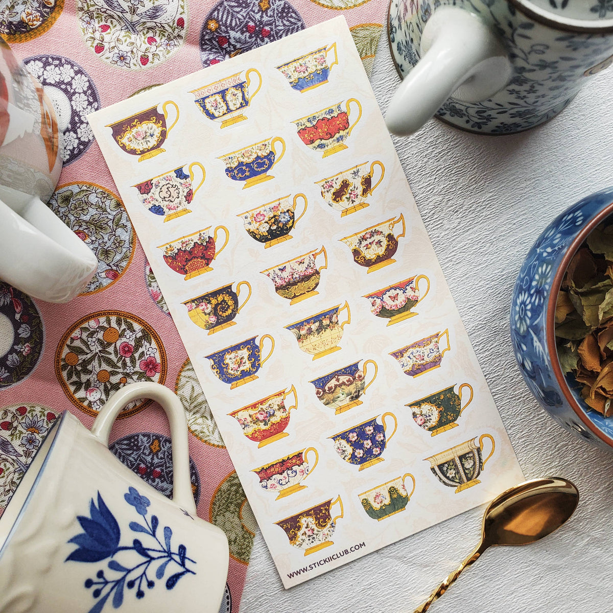 Sheet of decorative teacup stickers on a table with tea-making items.