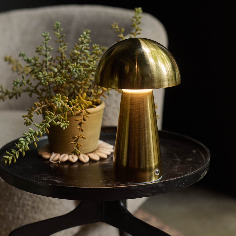 Gold mushroom lamp on a dark surface with plants in the background