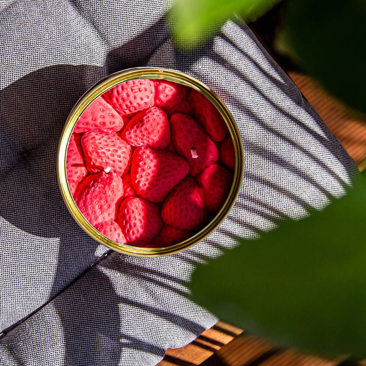 Can of red strawberries candle on a textured surface with shadows