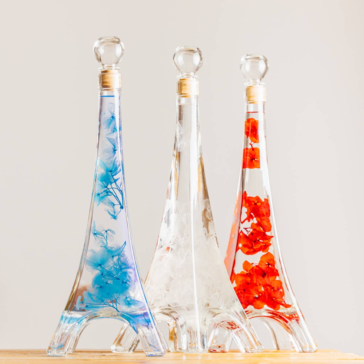 Three decorative glass bottles shaped as the eiffel tower with floral designs on a light background