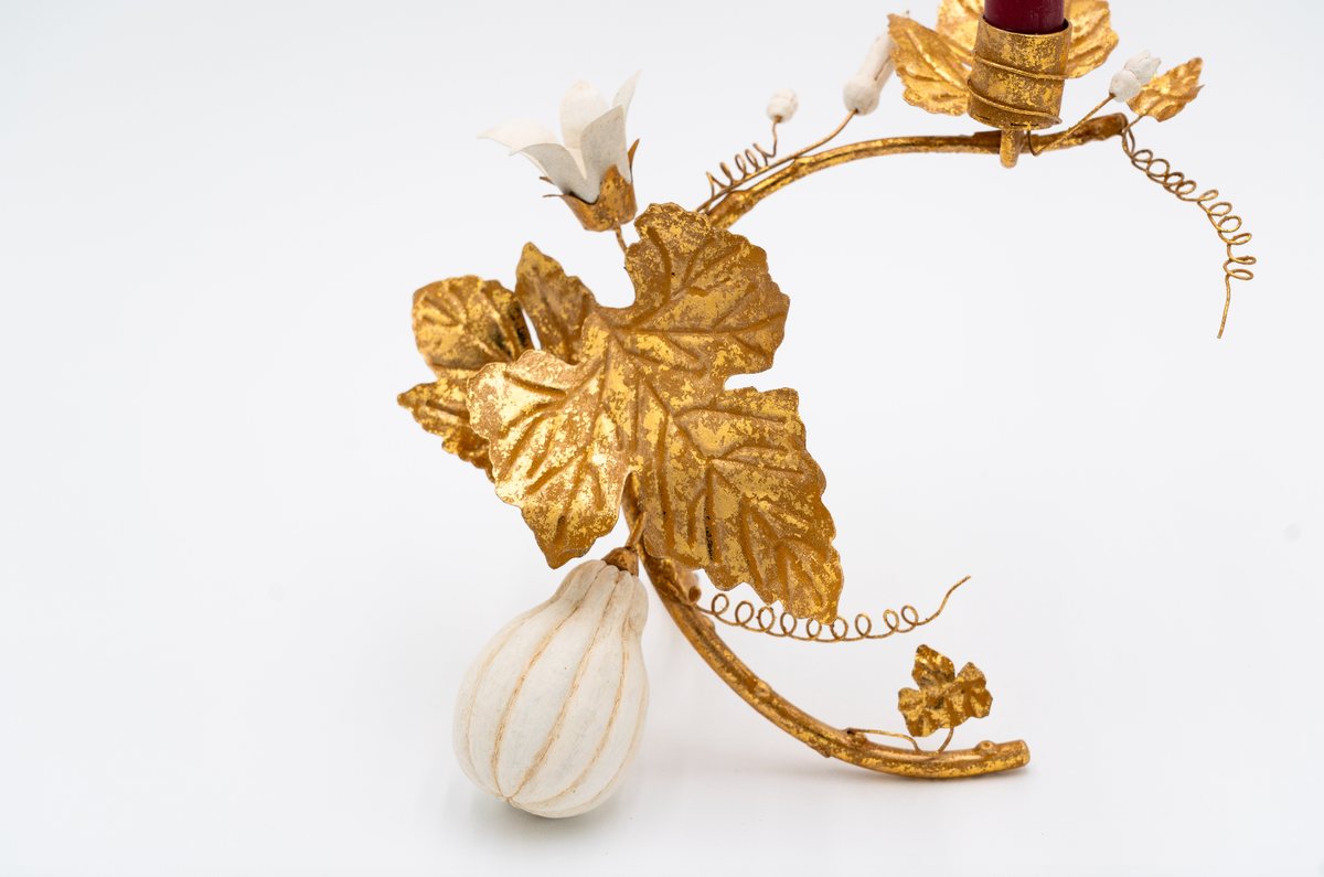 Close up of candle holder with gold leaves and a white gourd on a light gray background