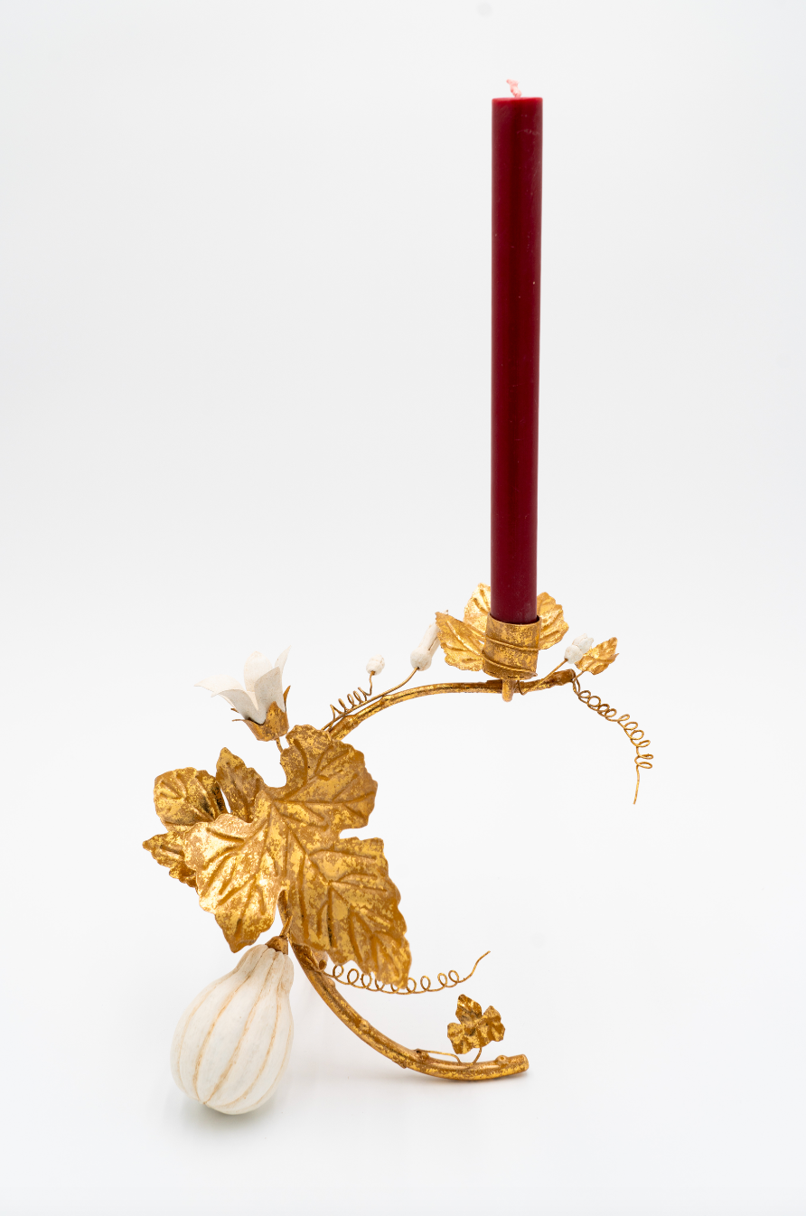 Decorative candle holder with gold leaf design and a red candle on a white background